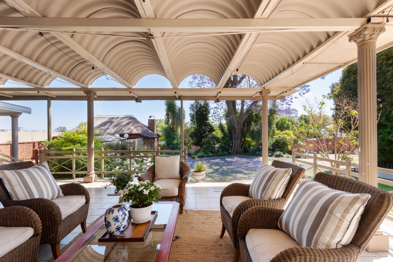 Covered veranda lounge with wicker armchairs overlooking the jacaranda garden at House Falcon Guesthouse